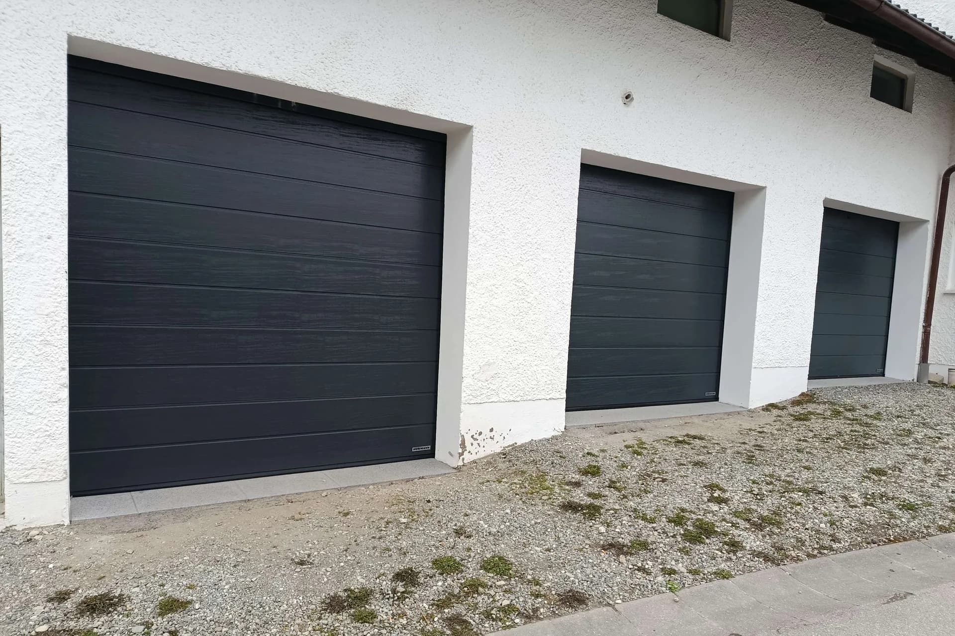 Drei anthrazitfarbene Sektionaltore an derselben Garage.