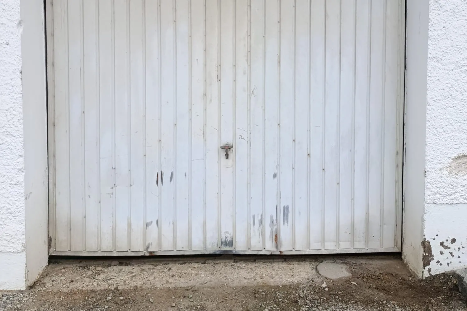 Altes weißes Garagentor mit sanierungsbedürftiger Laibung und beschädigtem Schwellenbereich vor der Garage.
