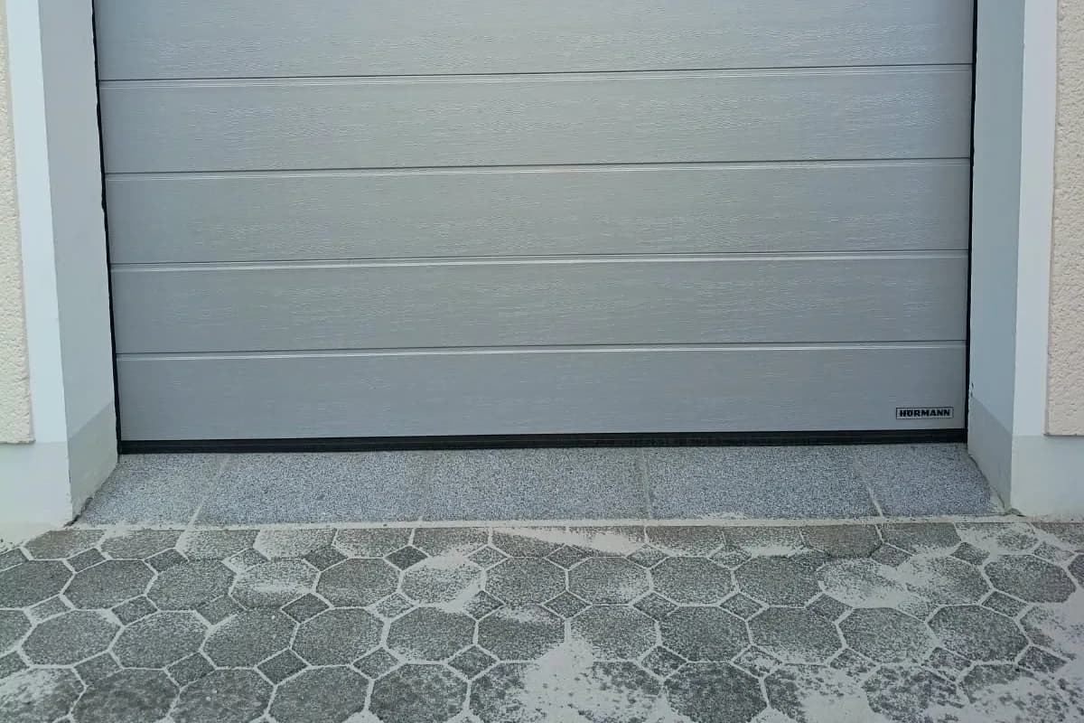 Sanierter Schwellenbereich unter einem grauen Garagentor mit angepasstem Betonpflaster.