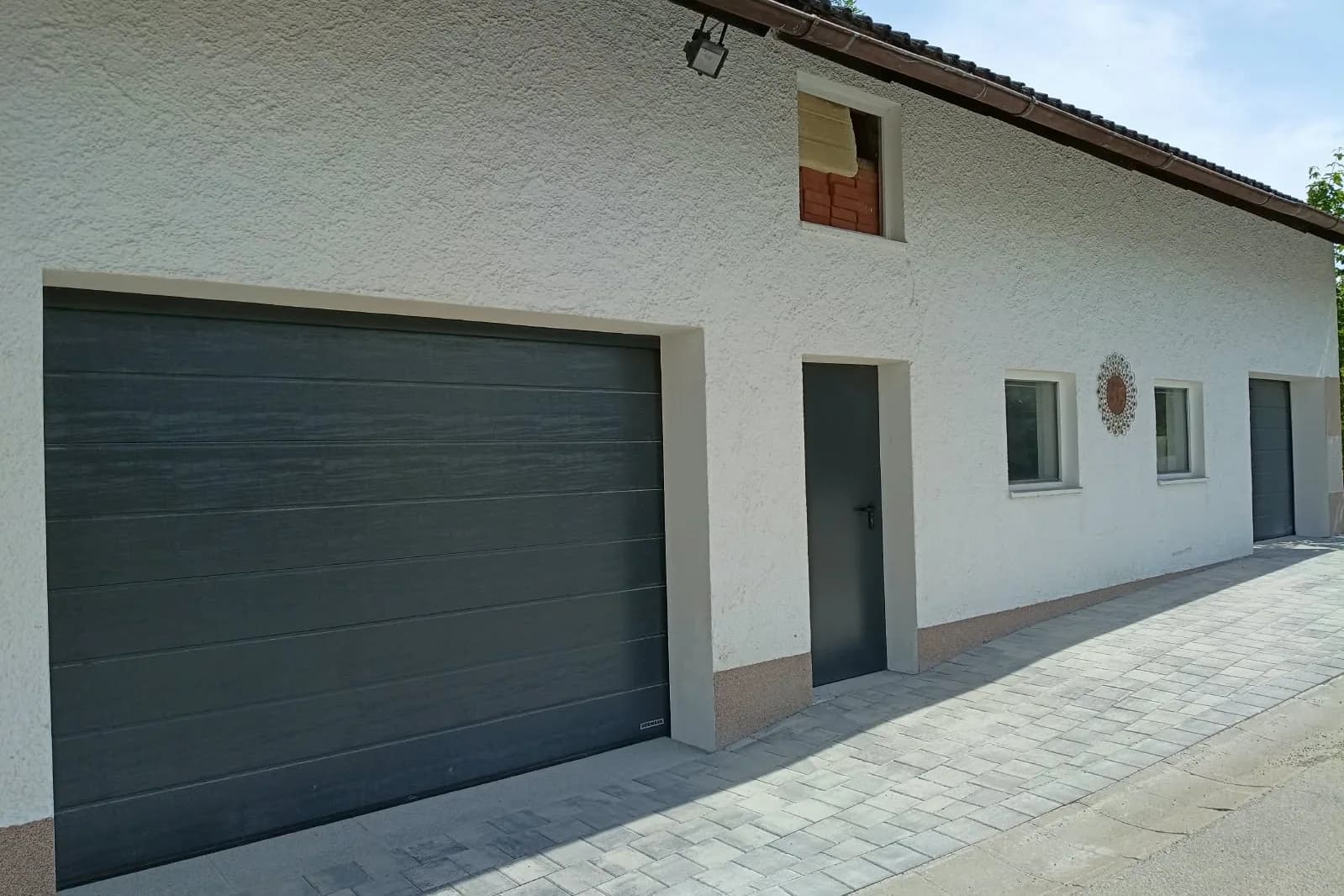 Modernisierte Gebäudeansicht in Ruhstorf an der Rott mit dunklem Garagentor, neuer Türe und sauber überarbeiteten Laibungen.